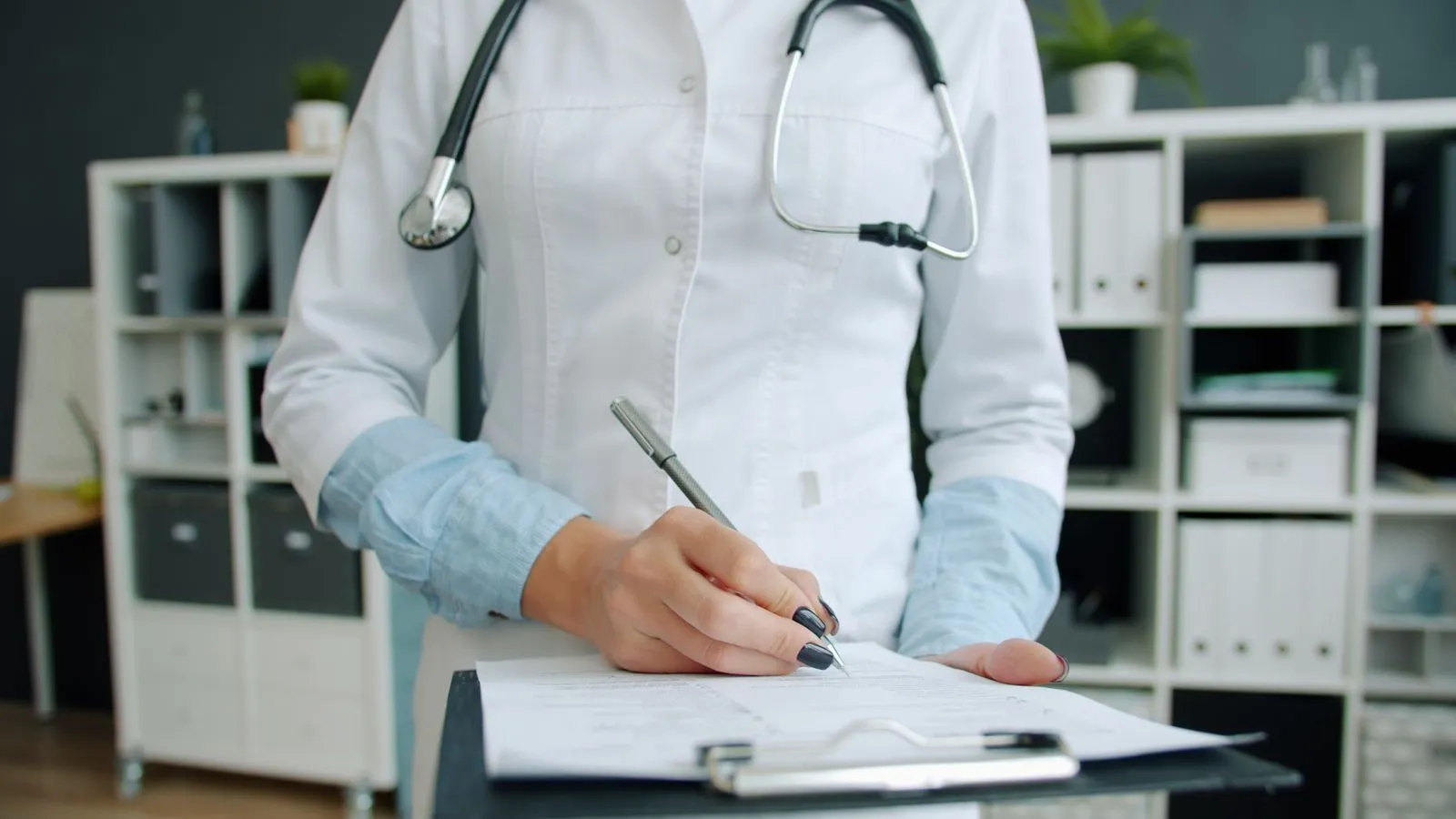 A doctor in a white coat writing notes on a clipboard in an office.